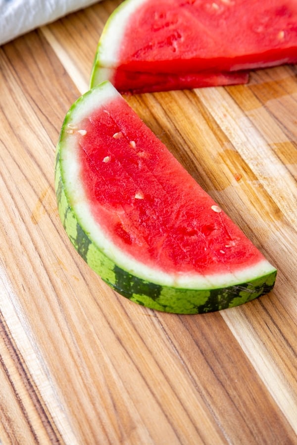 A slice of watermelon on a wood board.