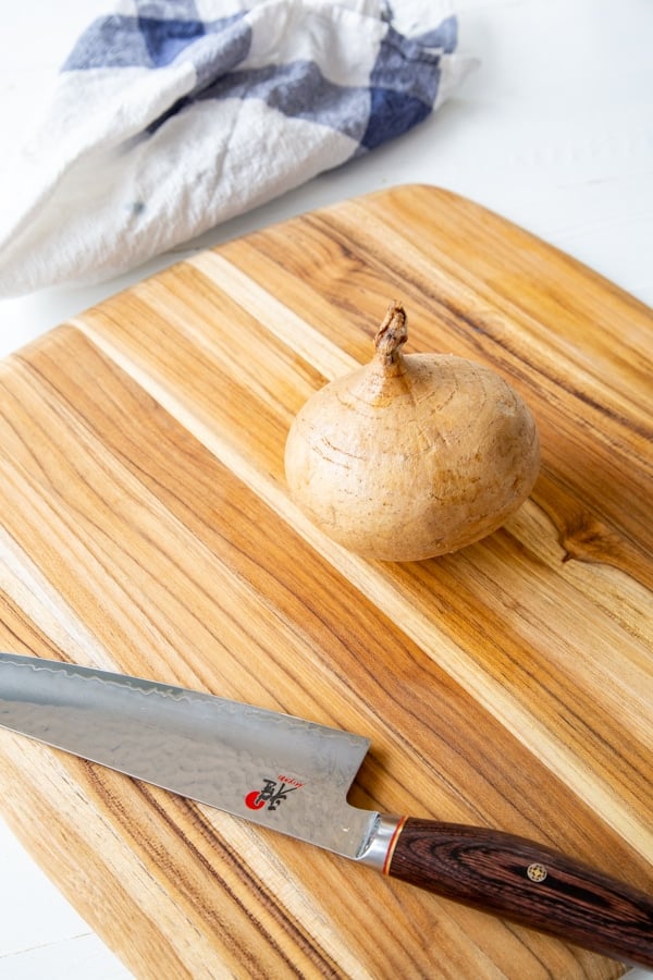 A whole unpeeled jicama on a wood board with a knife.