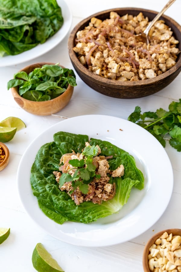 A lettuce leaf on a white plate with tofu veggies and basil leaves on top.