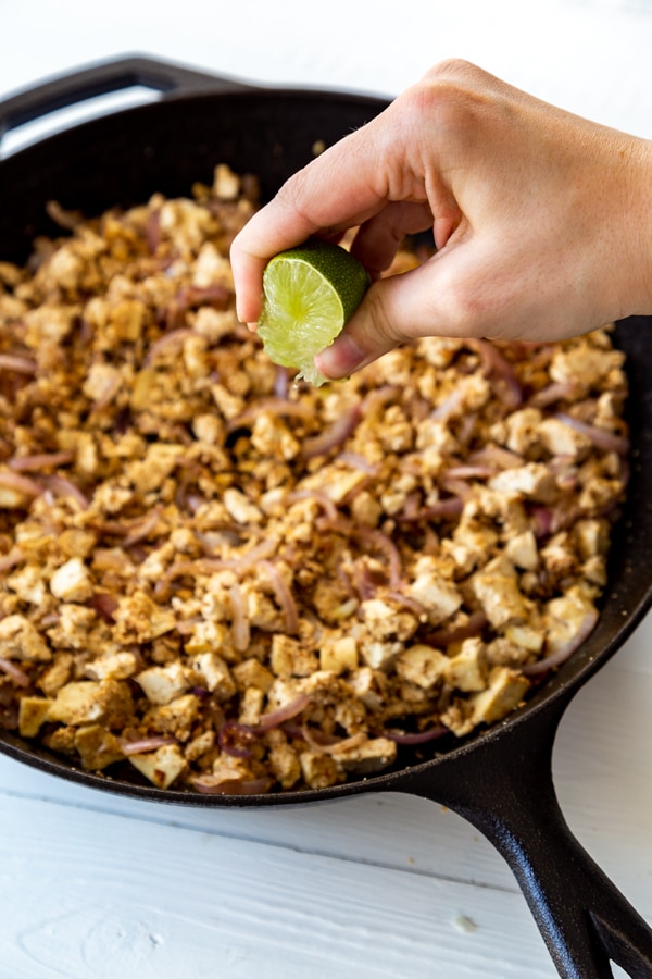 An iron skillet with a vegetable mixture and a hand squeezing a lime over the top.