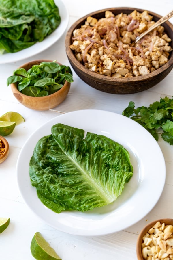 A lettuce leaf on a white plate with ingredients for a wrap next to it. 