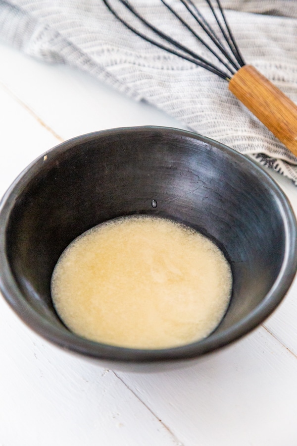 melted butter in a black bowl with a wood whisk next to it.