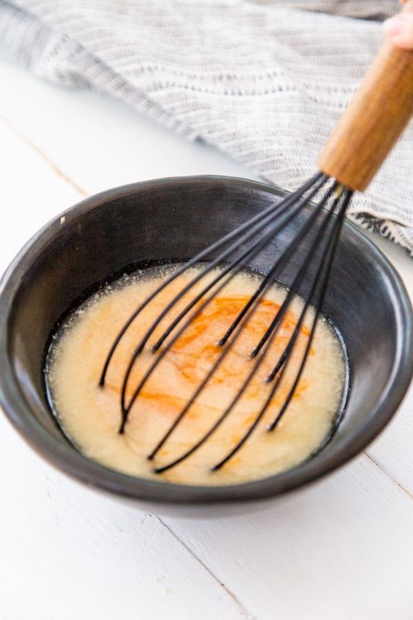 Melted butter and hot sauce in a black bowl being whisked together with a wood whisk.