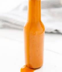 A bottle of buffalo sauce with sauce dripping down the side of the bottle.
