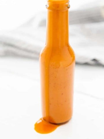 A bottle of buffalo sauce with sauce dripping down the side of the bottle.