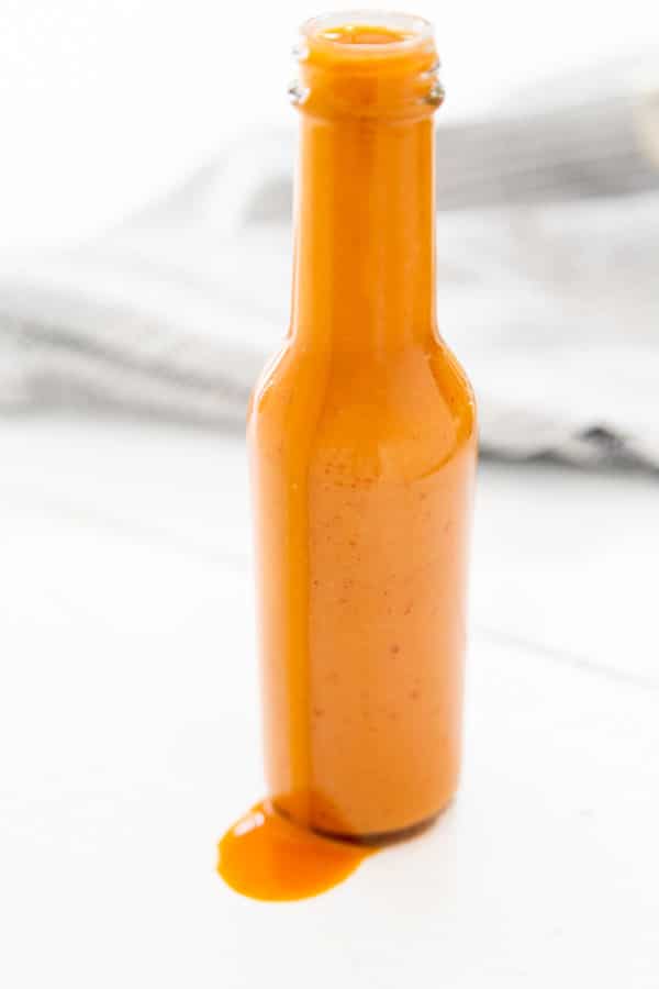 A bottle of buffalo sauce with sauce dripping down the side of the bottle.