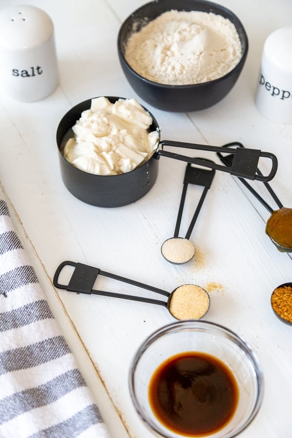 A white table with black measuring cups and spoons full of flour, tofu and spices.