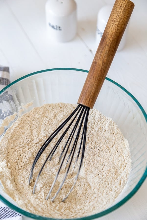 A glass bowl with flour and a wooden whisk.