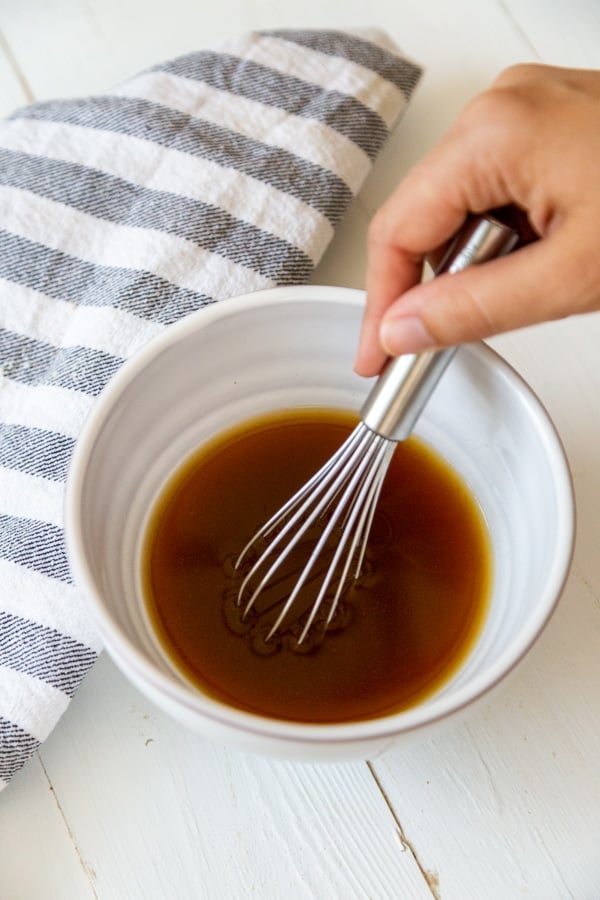 A hand whisking a bowl of brown liquid.