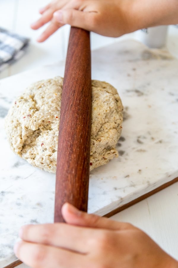 Hands rolling dough with a wooden rolling pin.