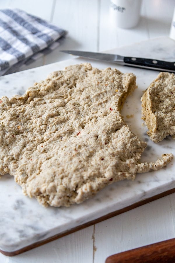 Seitan rolled out on a marble board with a piece cut out of it.