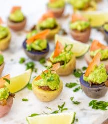 Potato taco bites on a marble board with a lime wedge and a glass of beer in the background.