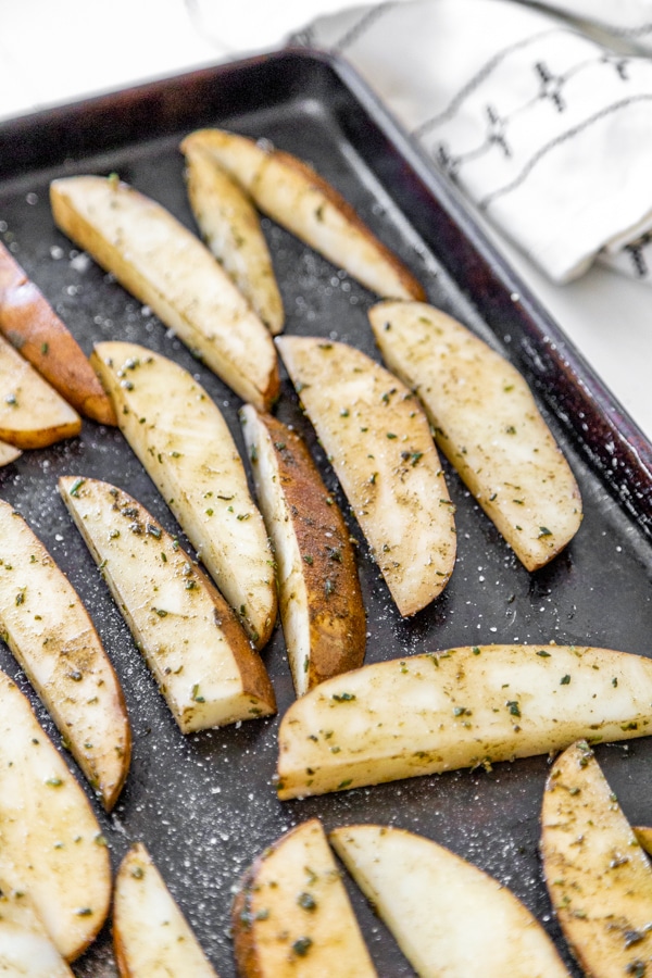 A baking sheet with sliced potatoes with herbs.