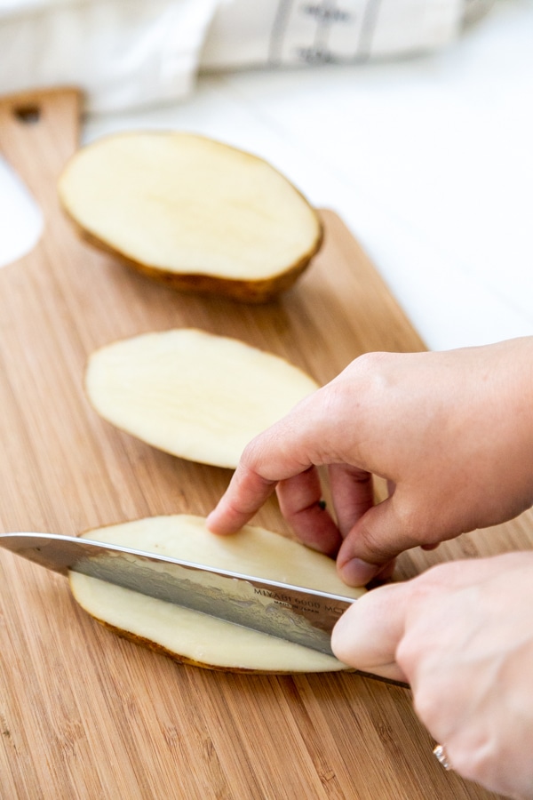 A hand slicing a potato into wedges.
