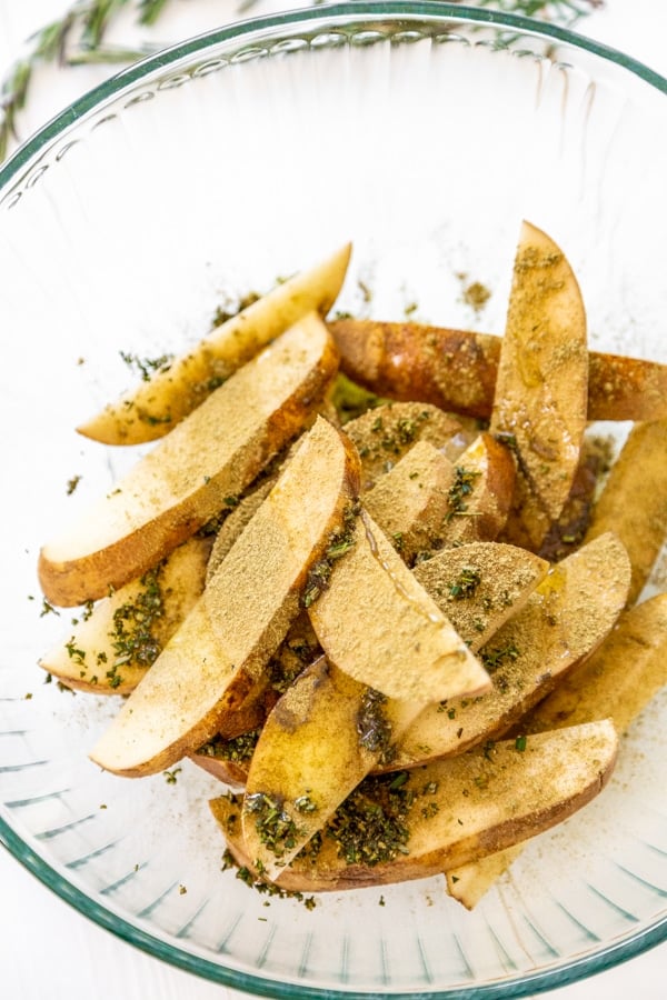 A pile of sliced potatoes in a bowl with olive oil and spices.