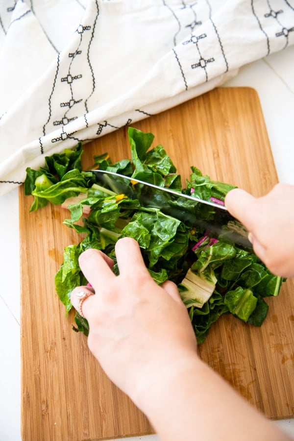 Hands chopping Swiss chard on a wood cutting board.