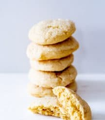 A stack of sugar cookies with on cut in half leaning on the stack.