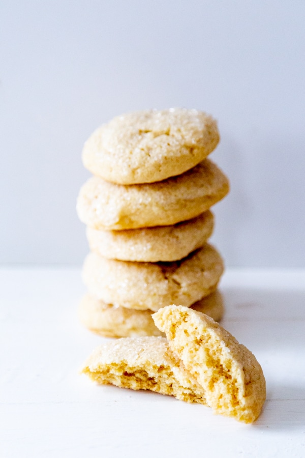 A stack of sugar cookies with on cut in half leaning on the stack.