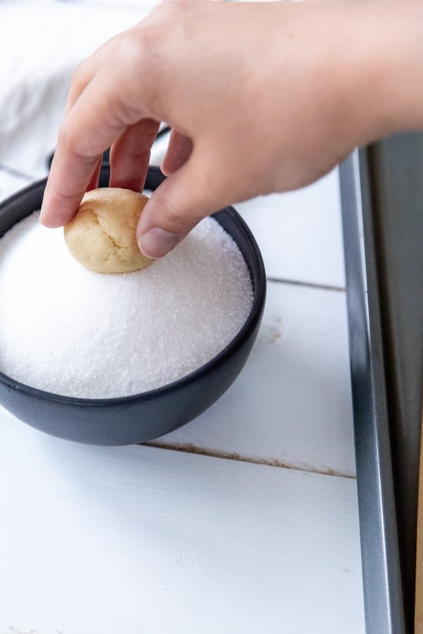 A hand rolling a ball of cookie dough in granulated sugar.