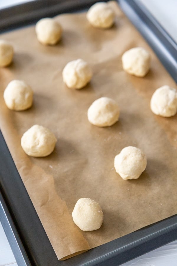 A baking sheet with parchment paper and unbaked sugar cookie balls.