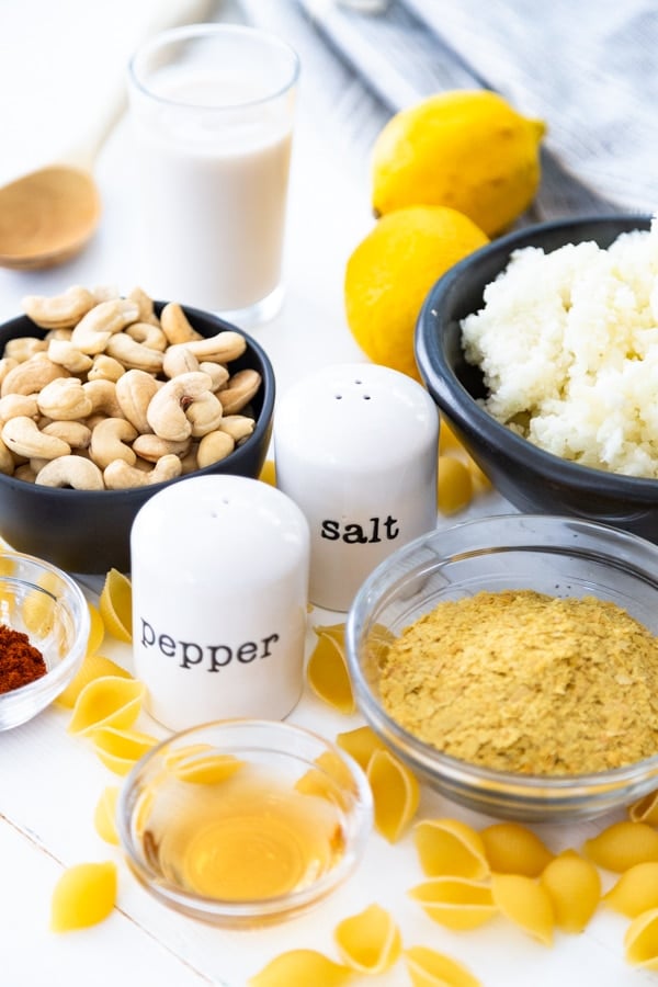 Bowls of ingredients for vegan mac and cheese on a white board.