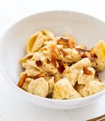 A white bowl with mac and cheese and coconut bacon sprinkled on top with a silver fork next to the bowl.