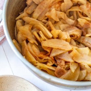 Chunky applesauce in a copper pan with a wooden spoon next to it.