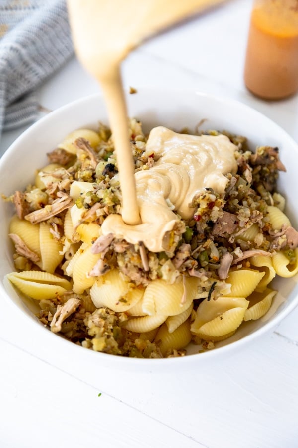 A white bowl with pasta, cheese sauce and sauteed vegetables