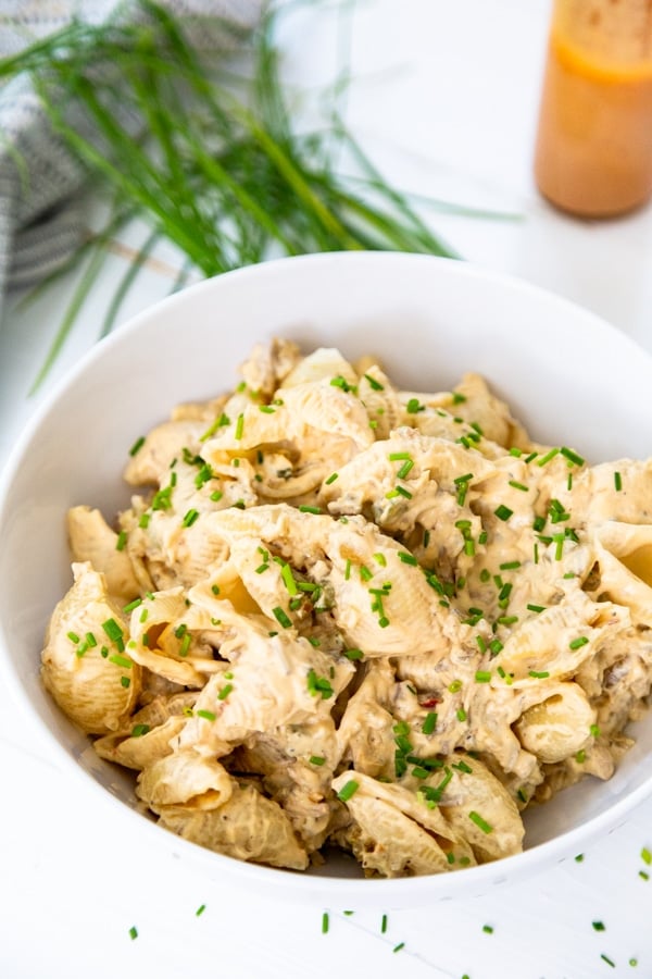 A white bowl of cheesy pasta with cilantro on top.