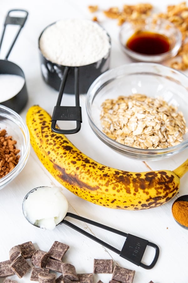 A banana, a bowl of oats, and measuring cups with flour and other ingredients for cookies. 