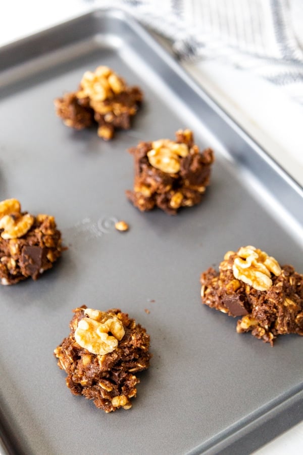 Chocolate cookie dough balls with a walnut in the center of each one on a baking sheet.