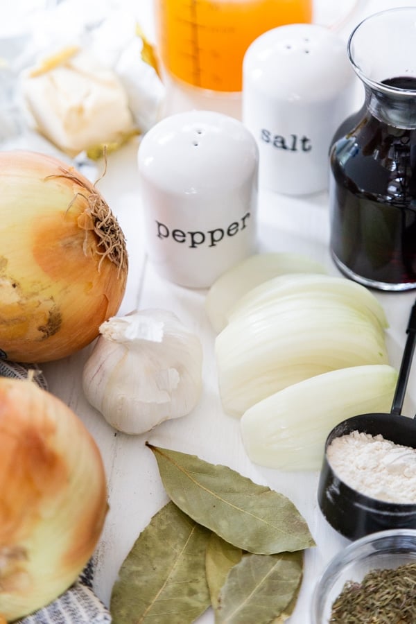 Ingredients for French onion soup on a white wood table.