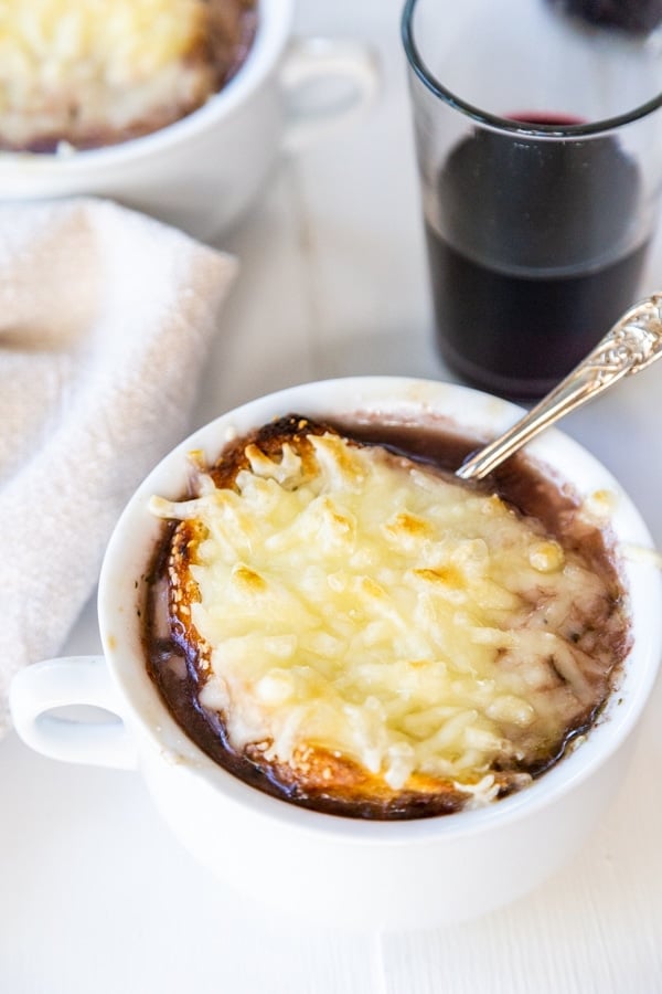 A bowl of French onion soup with melted cheese on top and a glass of red wine.