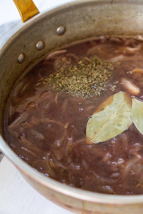 A copper pan with broth and onions and bay leaves.