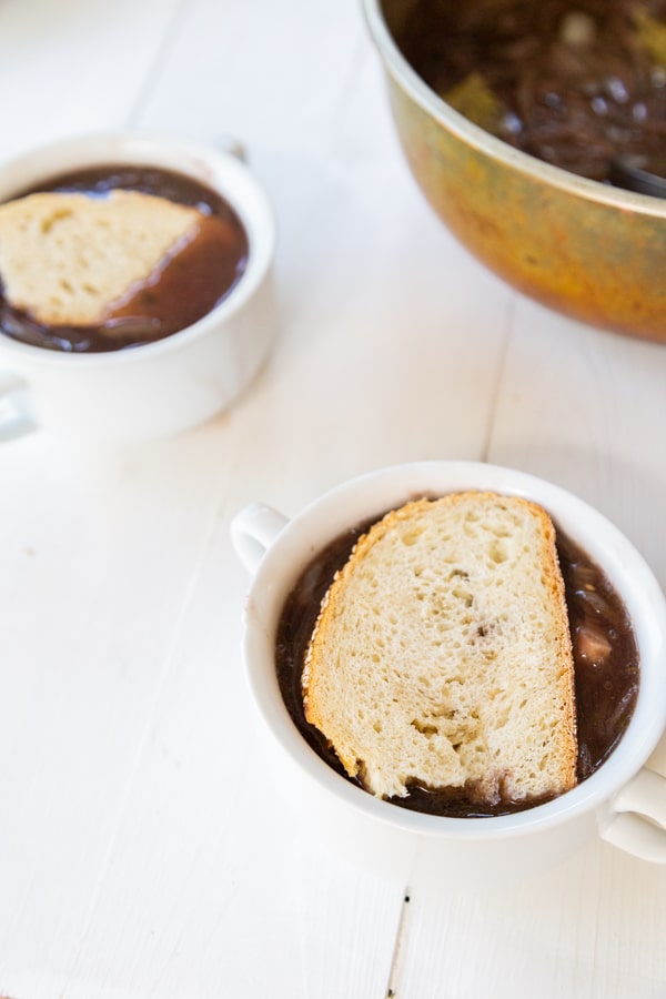 Two white bowls of onion soup with a slice of bread on top.