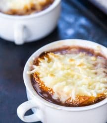 Two white bowls of French onion soup with melted cheese on top.