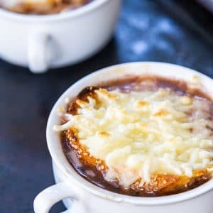 Two white bowls of French onion soup with melted cheese on top.