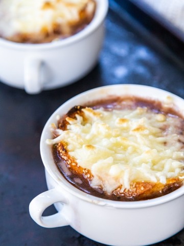 Two white bowls of French onion soup with melted cheese on top.