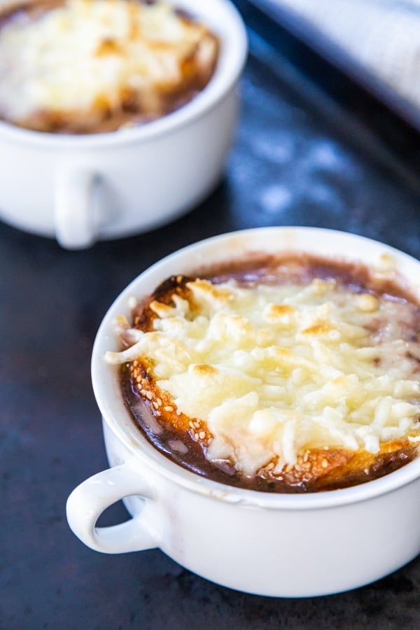 Two white bowls of French onion soup with melted cheese on top.