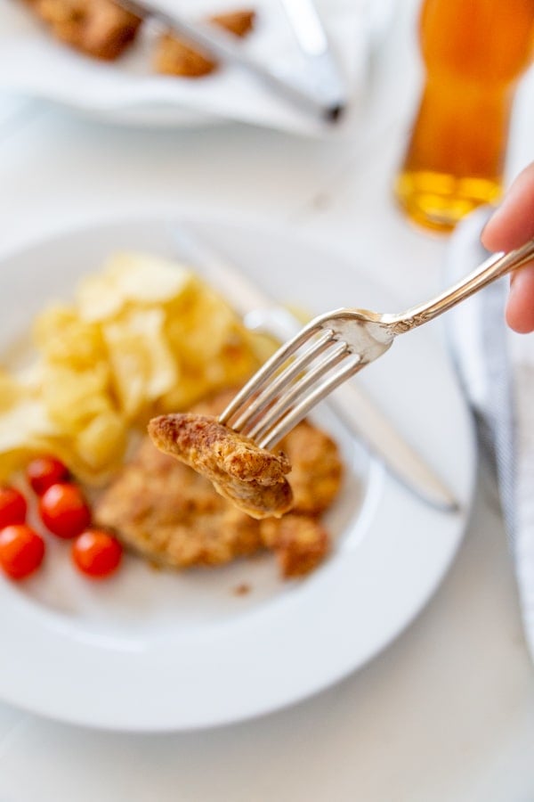 A hand cutting a piece of fried chicken with a fork. 