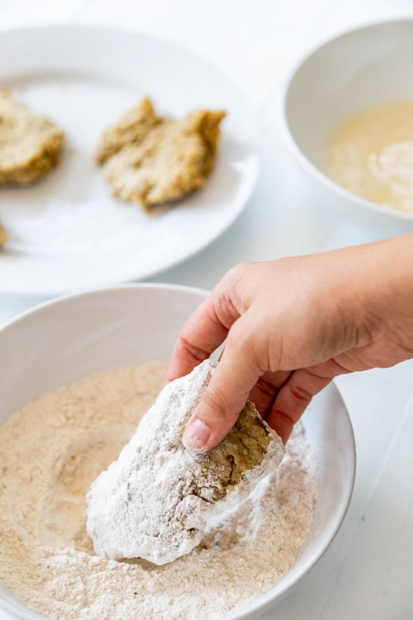 A hand dipping a chicken cutlet coated in flour and egg in more flour.