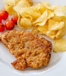 A piece of fried chicken, chips, and tomatoes on a white plate.