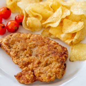 A piece of fried chicken, chips, and tomatoes on a white plate.