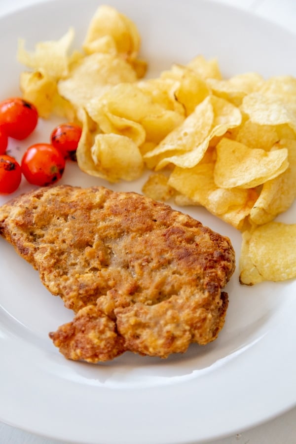 A piece of fried chicken, chips, and tomatoes on a white plate.