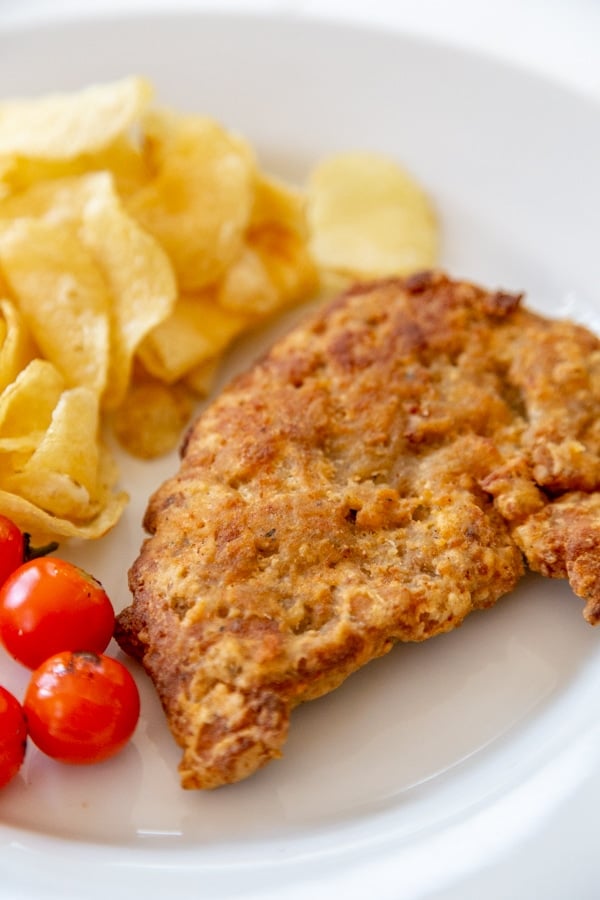 A piece of fried chicken, potato chips, and tomatoes on a white plate. 