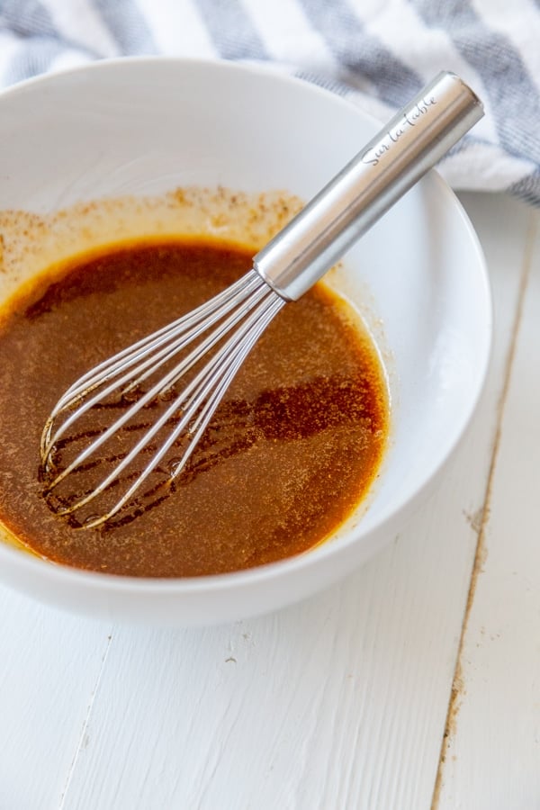 A white bowl with red sauce and a whisk.