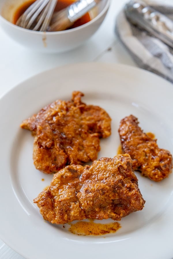 Spicy fried chicken on a white plate with the bowl of spicy sauce behind it. 