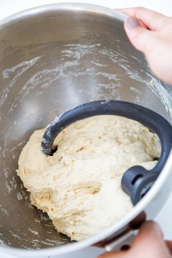 A ball of pizza dough in a silver mixing bowl with a break hook attachment.