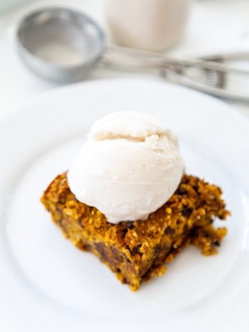 A chocolate chip blondie on a white plate with a scoop of ice cream on top.