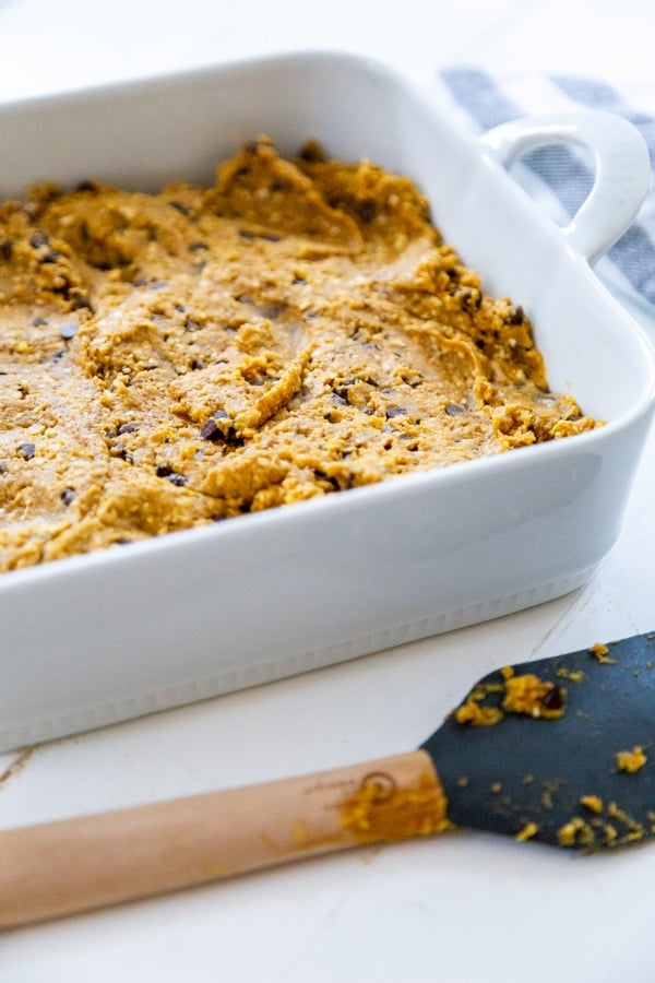 A white ceramic cake pan with pumpkin chocolate chip blondie batter and a spatula.